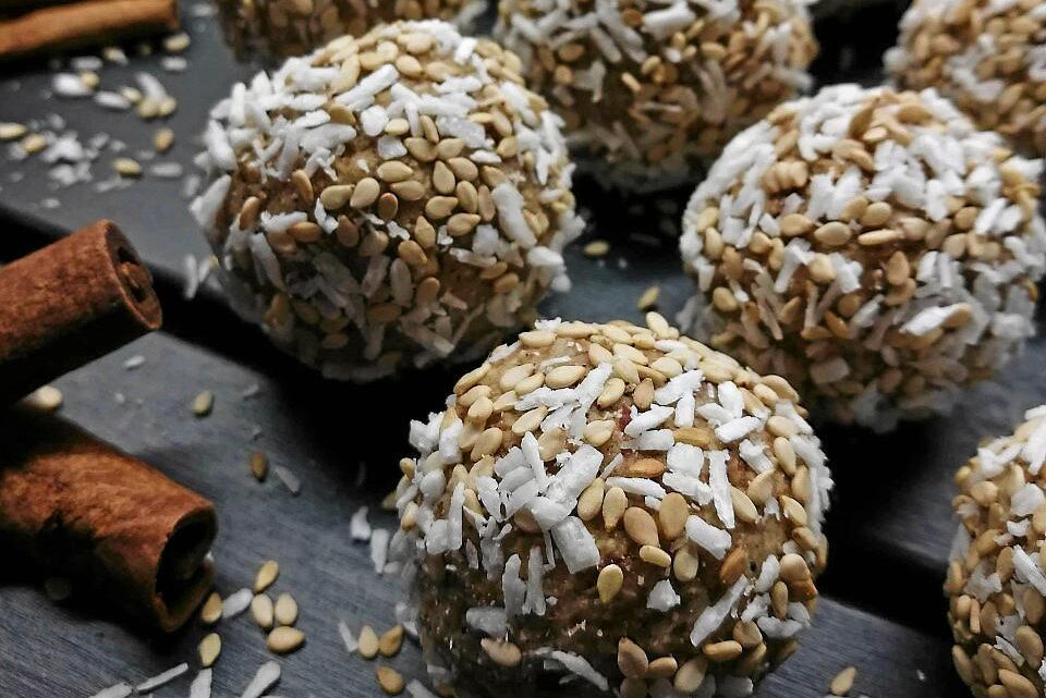 Närbild på hemmagjorda energibollar med kokos och sesamfrön, bredvid kanelstänger