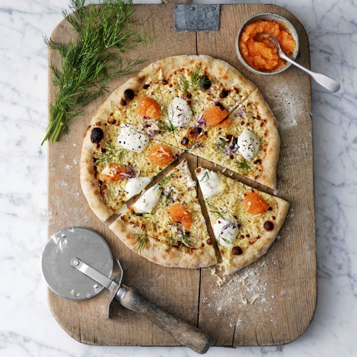 Tunn pizza med crème fraiche, rödlök och klickar av orange fiskrom på skärbräda