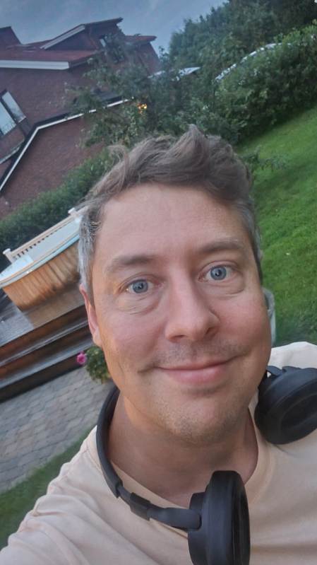 Leende Fredrik Rinsén i trädgård framför ett hus i kvällsljus
