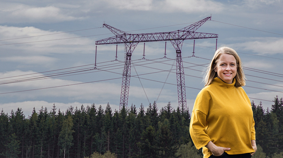 Kvinna i gul tröja står vid skog med höga elledningar i bakgrunden