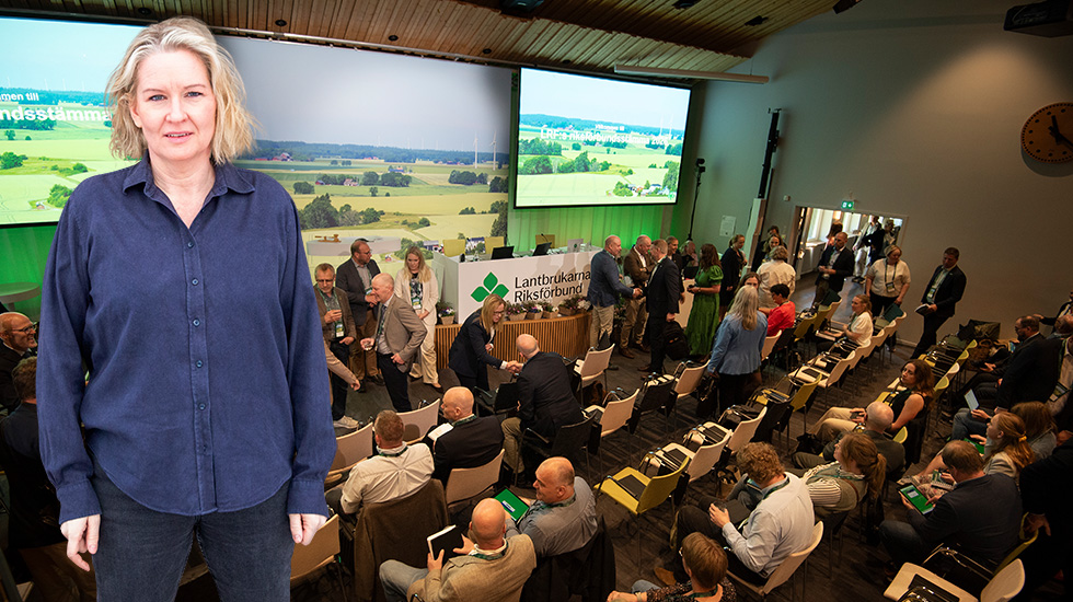 Kvinna framför bild av fullsatt konferenssal med lantbrukstema på scenen