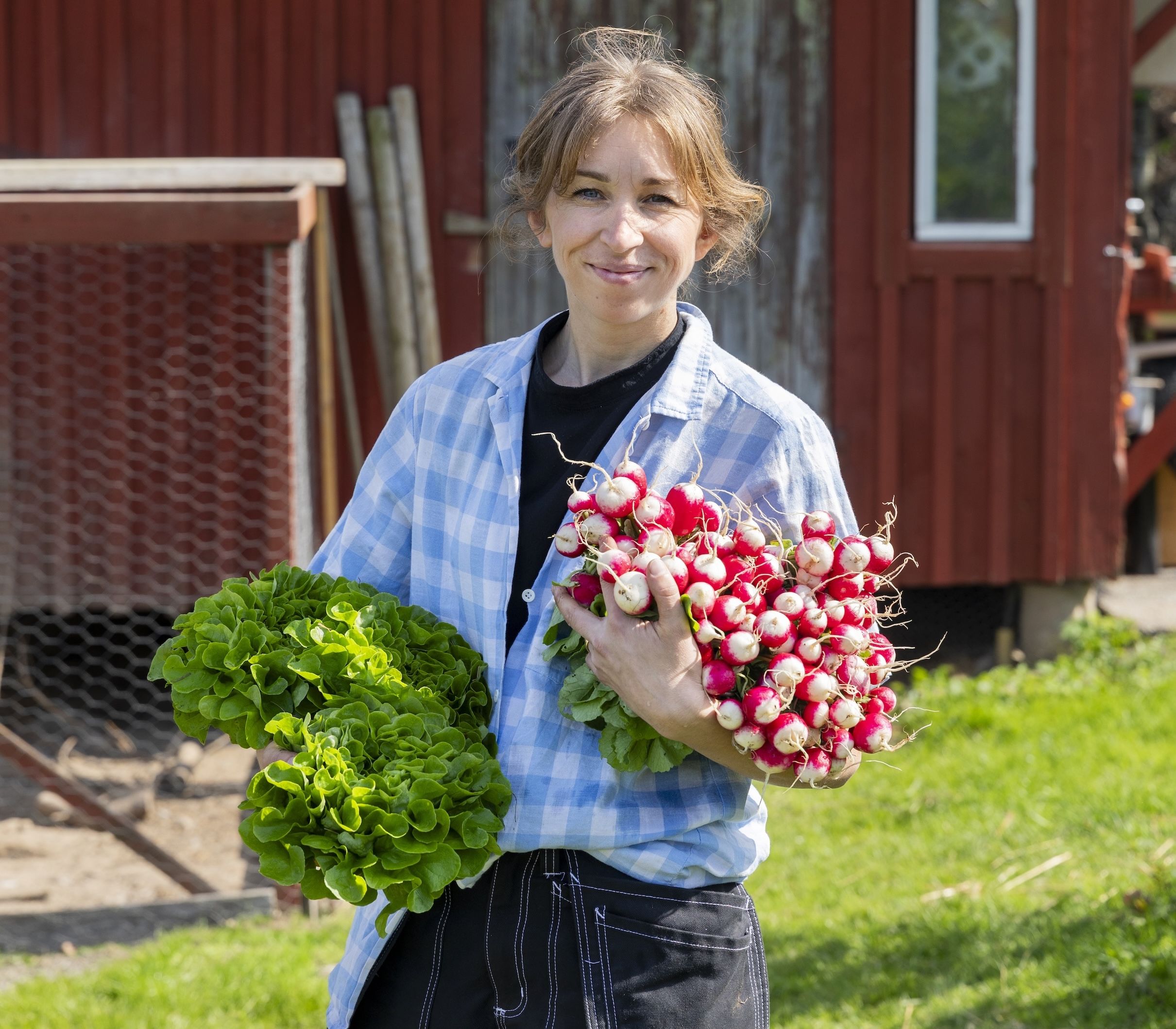 Leende person på gård som håller sallad och knippen med rädisor