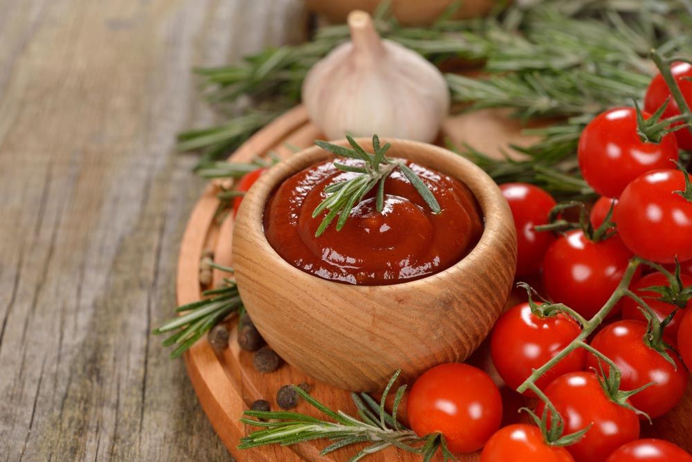 Skål med tomatsås och rosmarin omgiven av körsbärstomater och vitlök