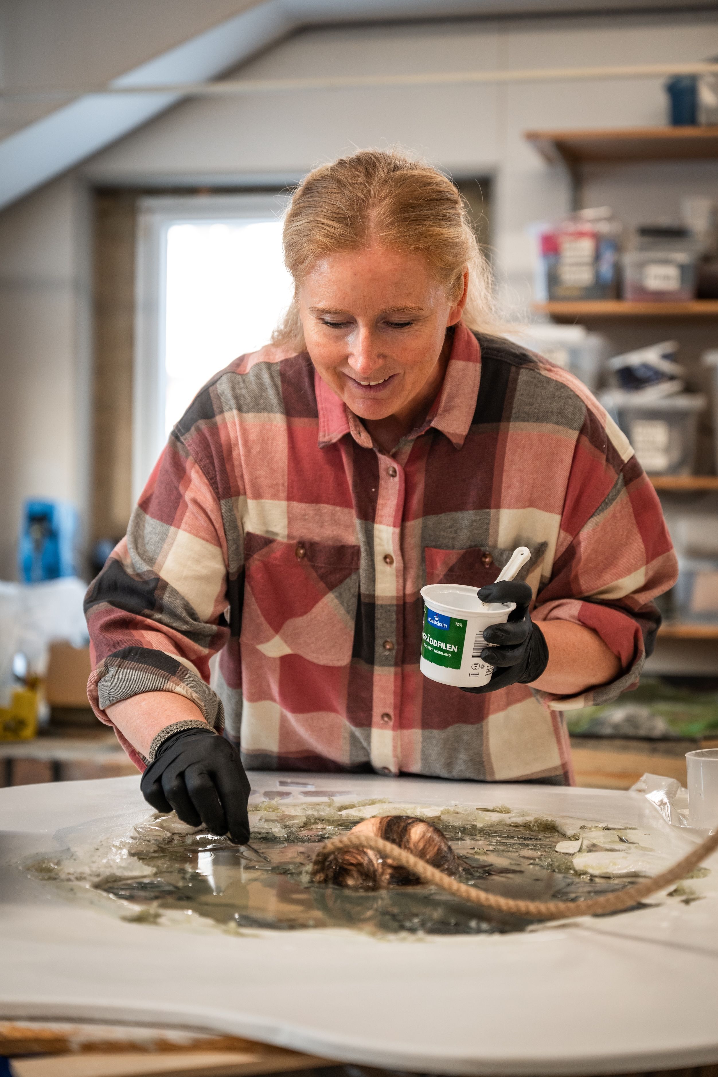 Eva-Karin i verkstad arbetar koncentrerat med ett konstverk på bordet