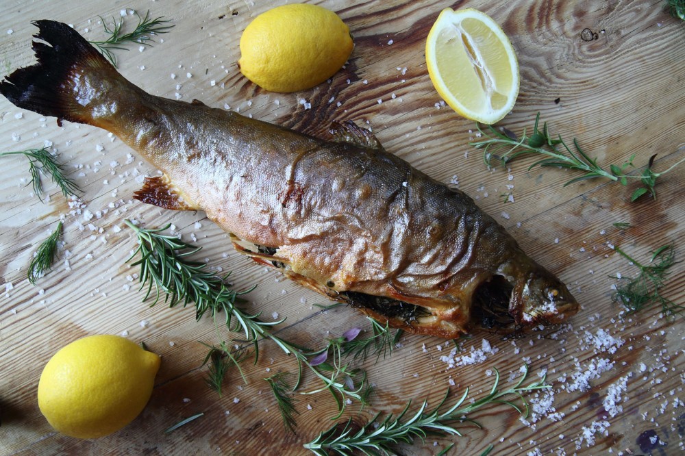 Helstekt fisk på träbord med citron, rosmarin och strödd havssalt runtomkring