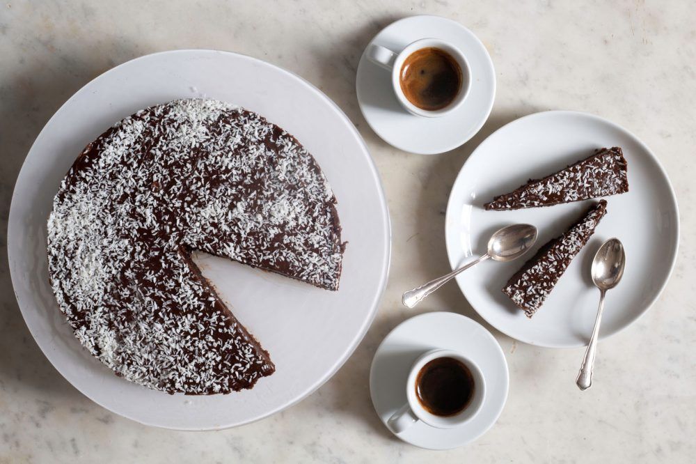 Rund kärlekmumskaka med kokos på fat, uppskuren i bitar med kaffe i koppar bredvid