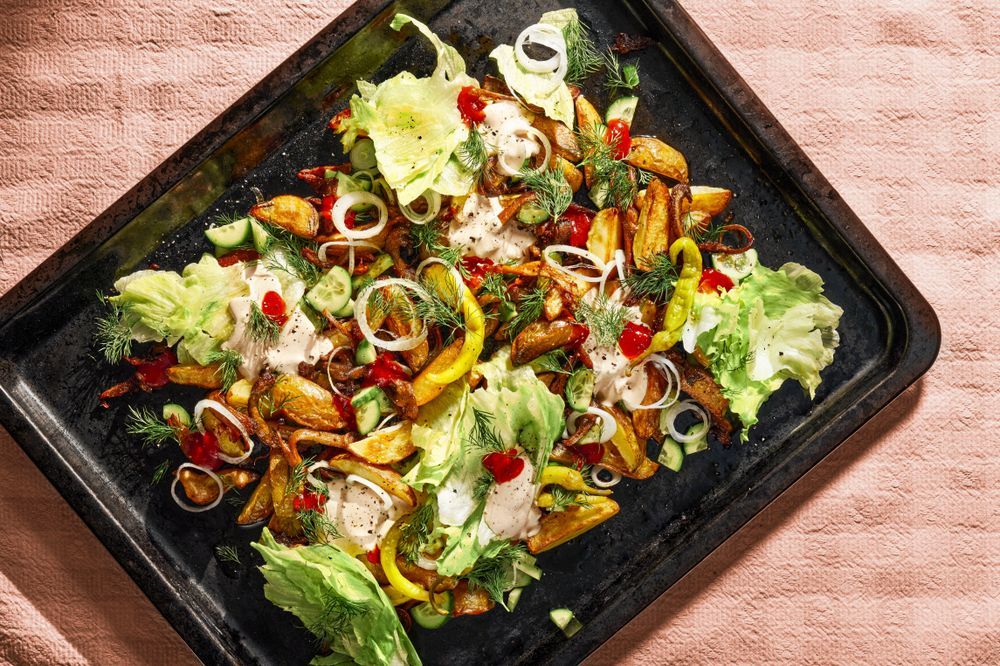 Ugnsrostad potatis med sallad och dressing på en svart plåt.