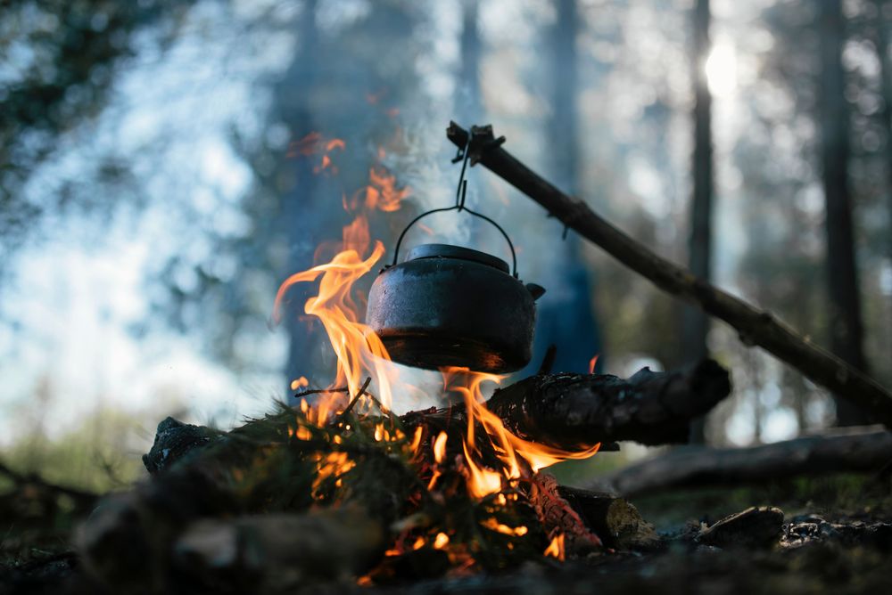 Kaffepanna hänger över öppen eld i skogsmiljö.