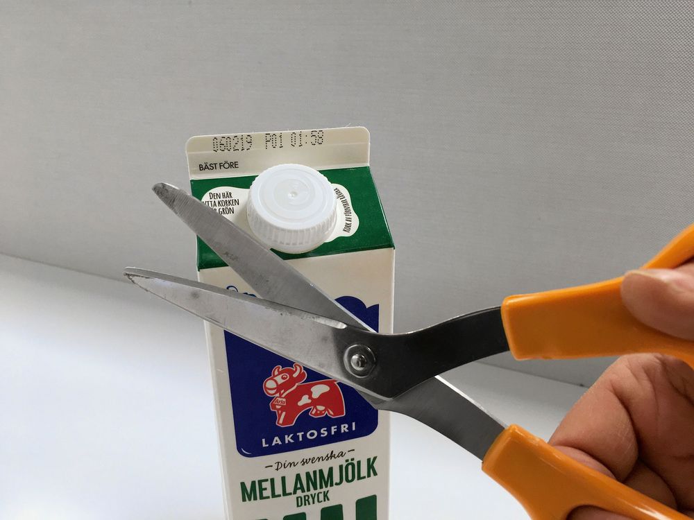 Person ur bild håller upp en sax framför en mjölktetra med plastkork.