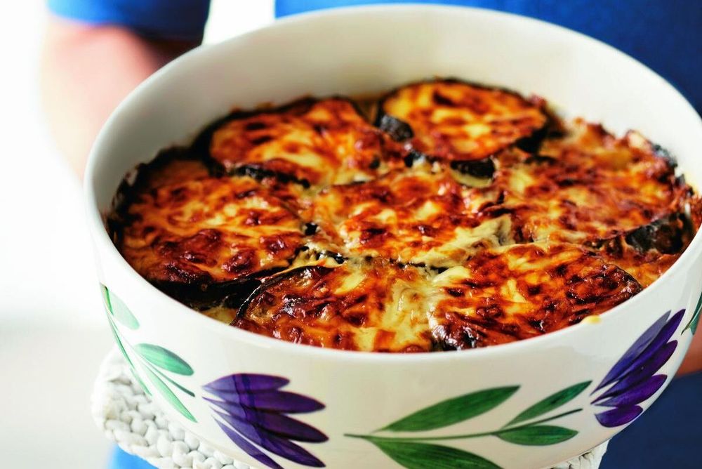 Person håller en ugnsform med gratinerad aubergine- och ostgratäng.
