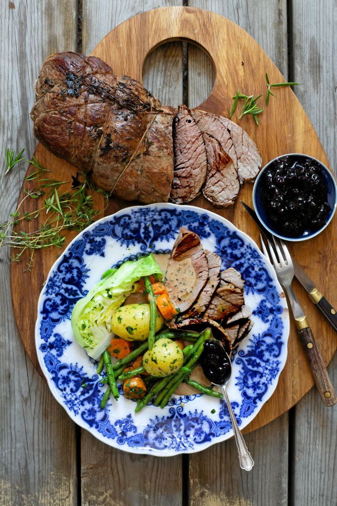Älgstek skärbräda intill tallrik med älgstek, potatis och grönsaker.