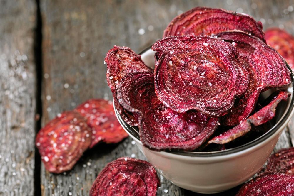 Skål med rödbetschips strösslade med salt på rustikt träbord