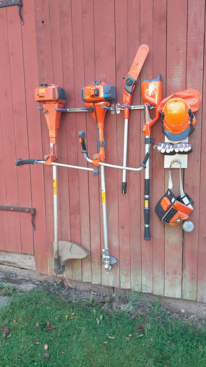 Orange trädgårdsredskap och skyddsutrustning upphängda på en röd trävägg