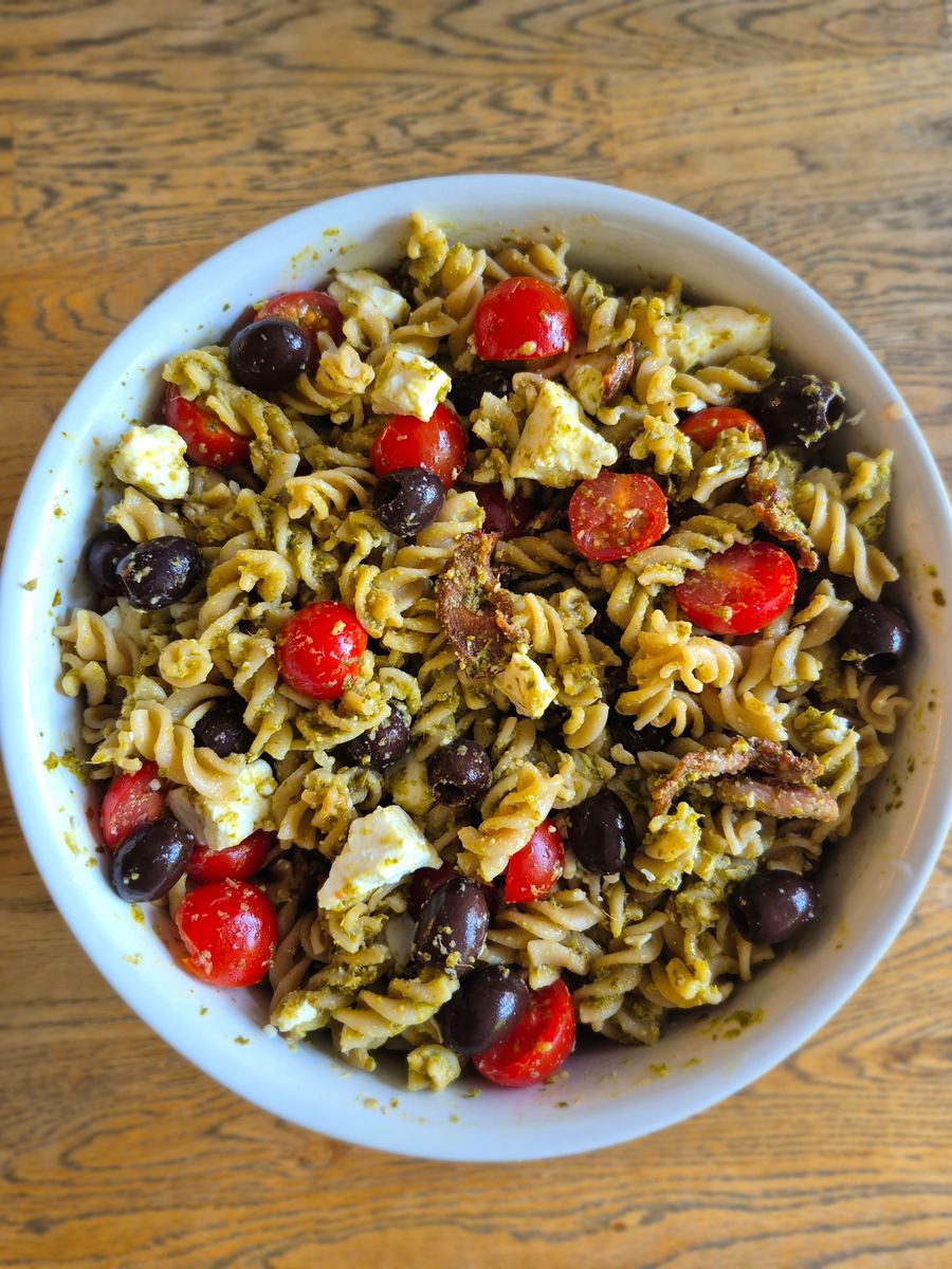 Stor karott med pastasallad med grön pesto, körsbärstomater, bacon, svarta oliver och fetaost.