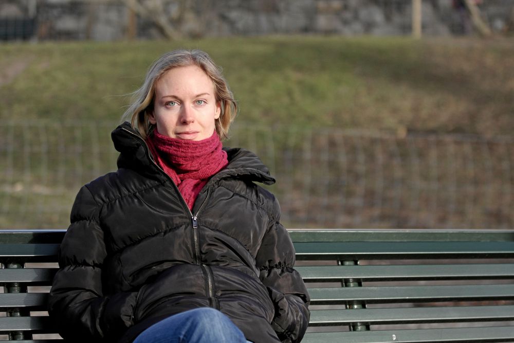 Erika Lindquist i mörk jacka sitter på parkbänk i en park en kylig dag, hon har OCD