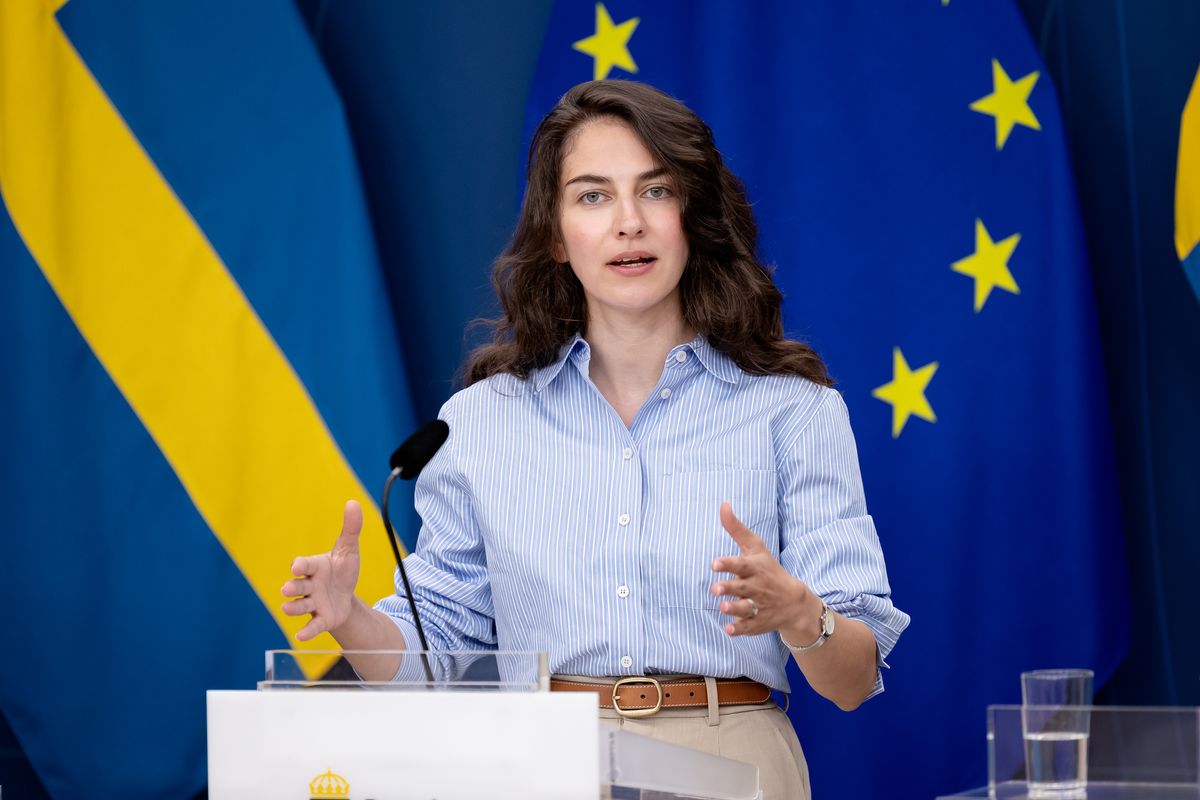 Kvinna håller presskonferens vid podium framför svenska och EU-flaggor