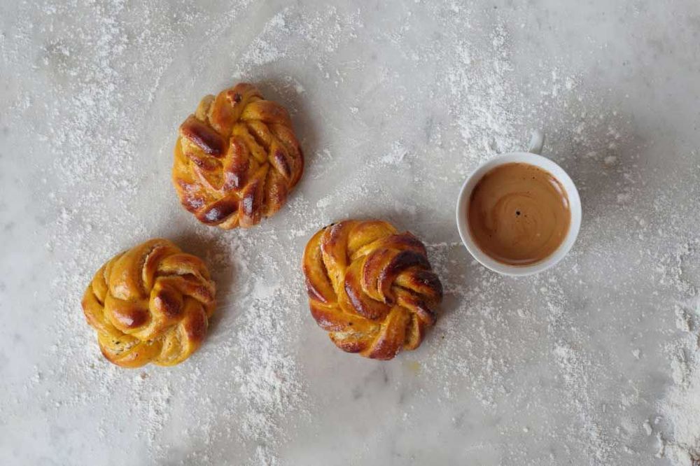 Tre lussebullar och en kopp kaffe på ett mjölat bord.