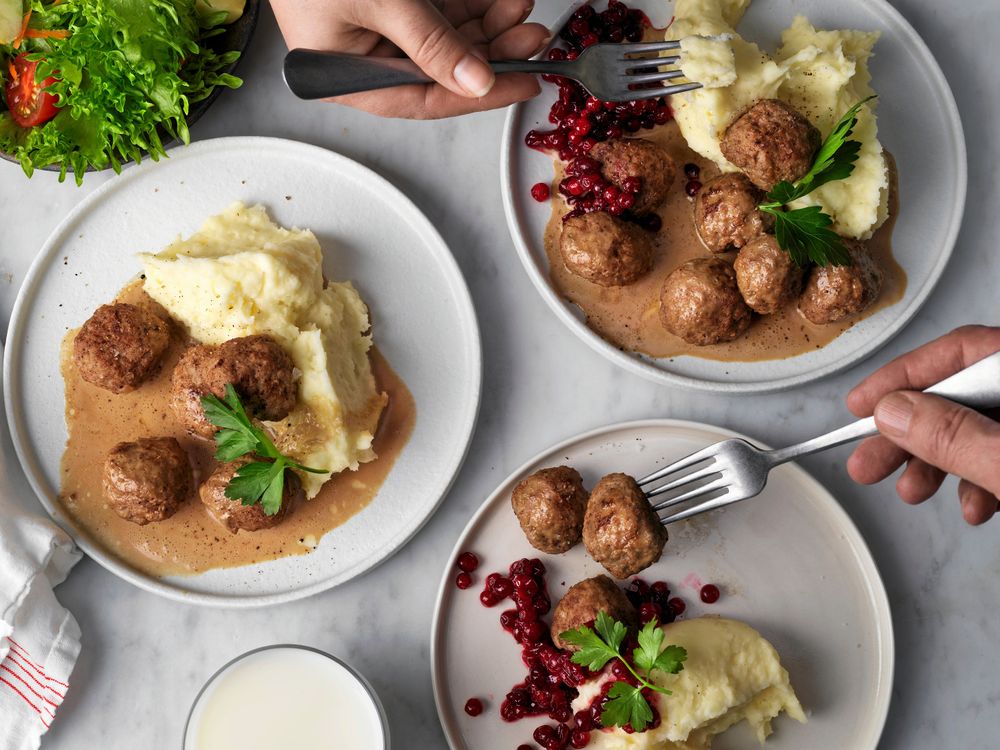 Köttbullar med potatismos, lingon och sås på tallrikar.