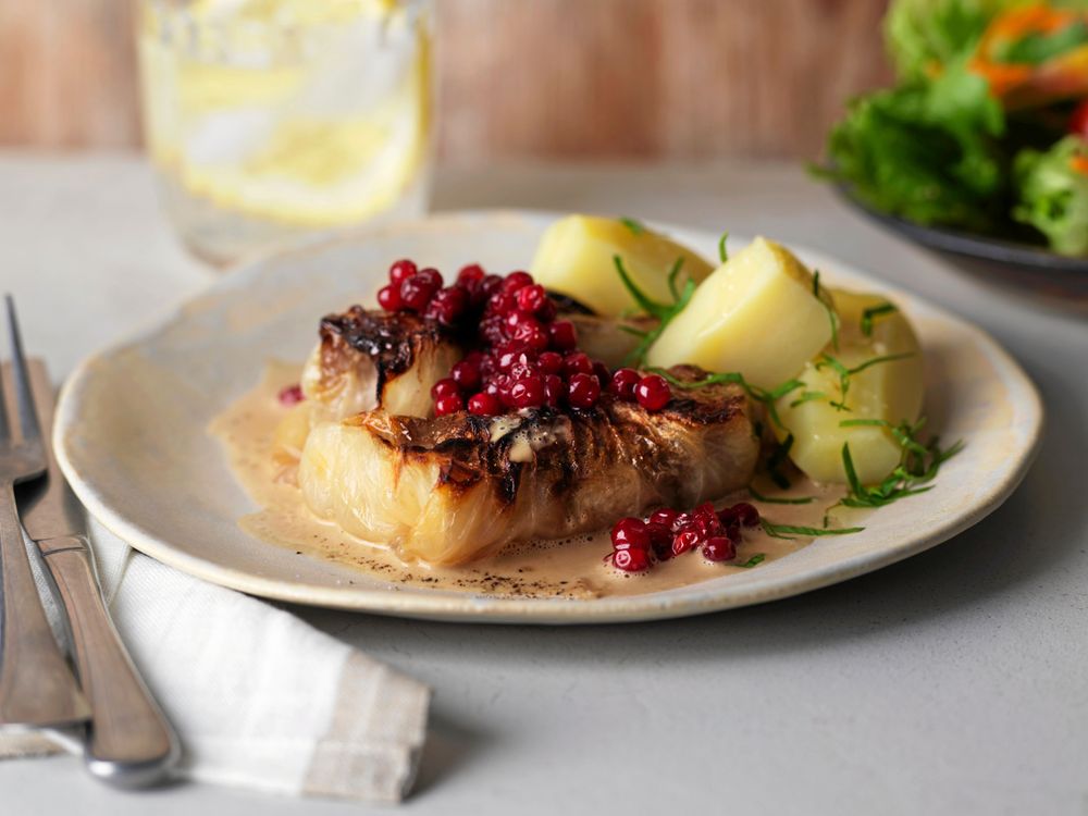 Tallrik med kåldolmar, kokt potatis, lingon och gräddsås på ljus duk