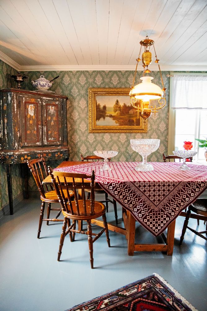 Salens gammeldags inredning med antikt skåp, rejält slagbord och gröna, mönstrade tapeter i 1800-talsstil.