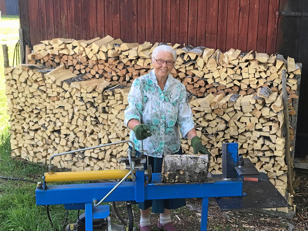 Märta Karlsson med sin vedklyv. Högen bakom henne kan tyckas stor, men utgör bara en tredjedel av vinterförrådet.