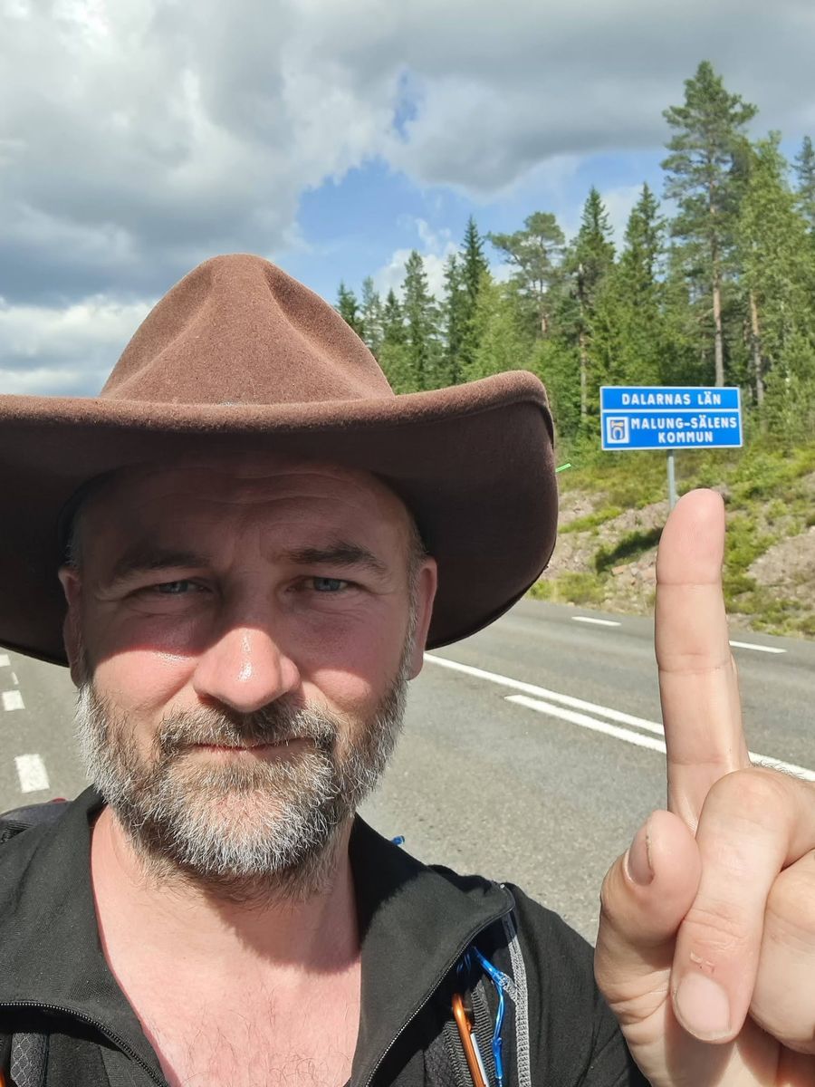 Man med hatt pekar på vägmärke vid infarten till Malung-Sälens kommun i Dalarna