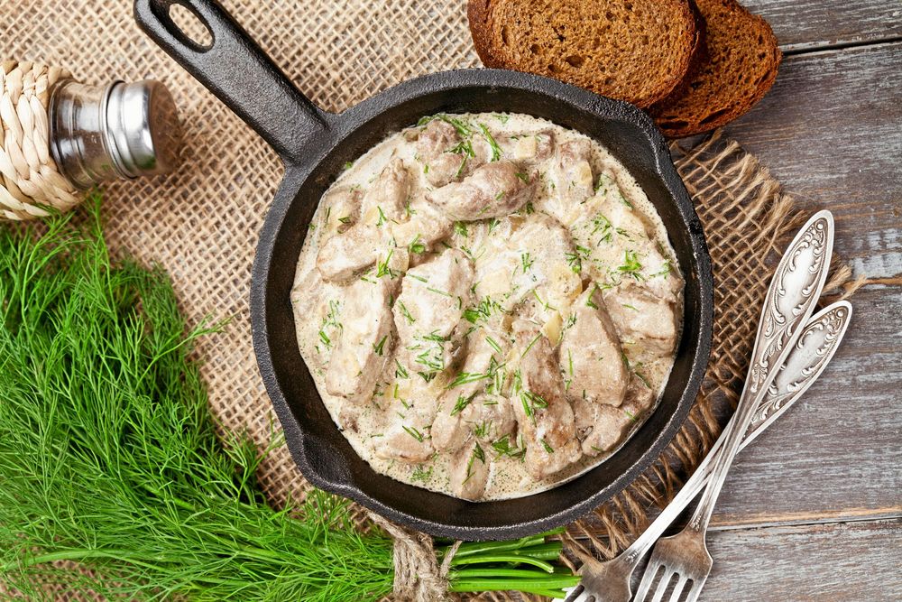 Gryta med kött i gräddsås och dill i gjutjärnspanna på rustikt träbord