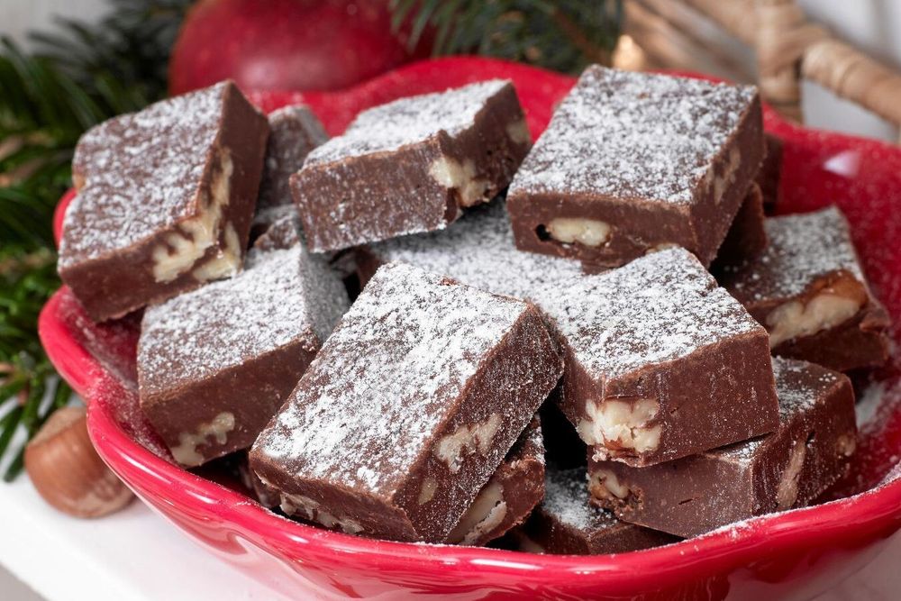 Närbild på chokladfudge med nötter, pudrad med florsocker på röd tallrik