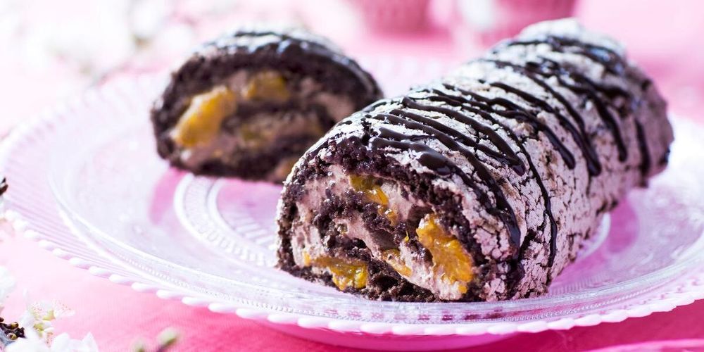 Chokladrulltårta med grädde och frukt på glasfat, dekorerad med chokladsås