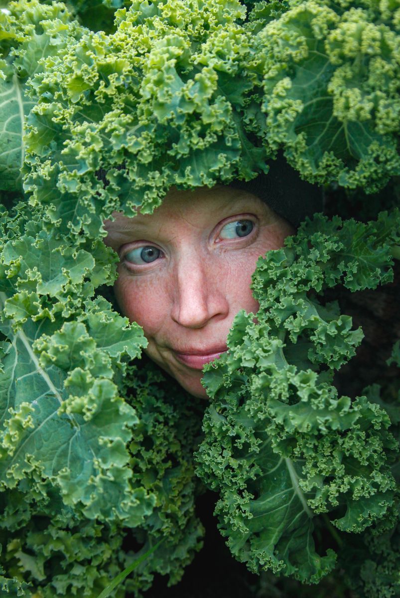 Anne Sandlund tittar genom täta grönkålsblad.