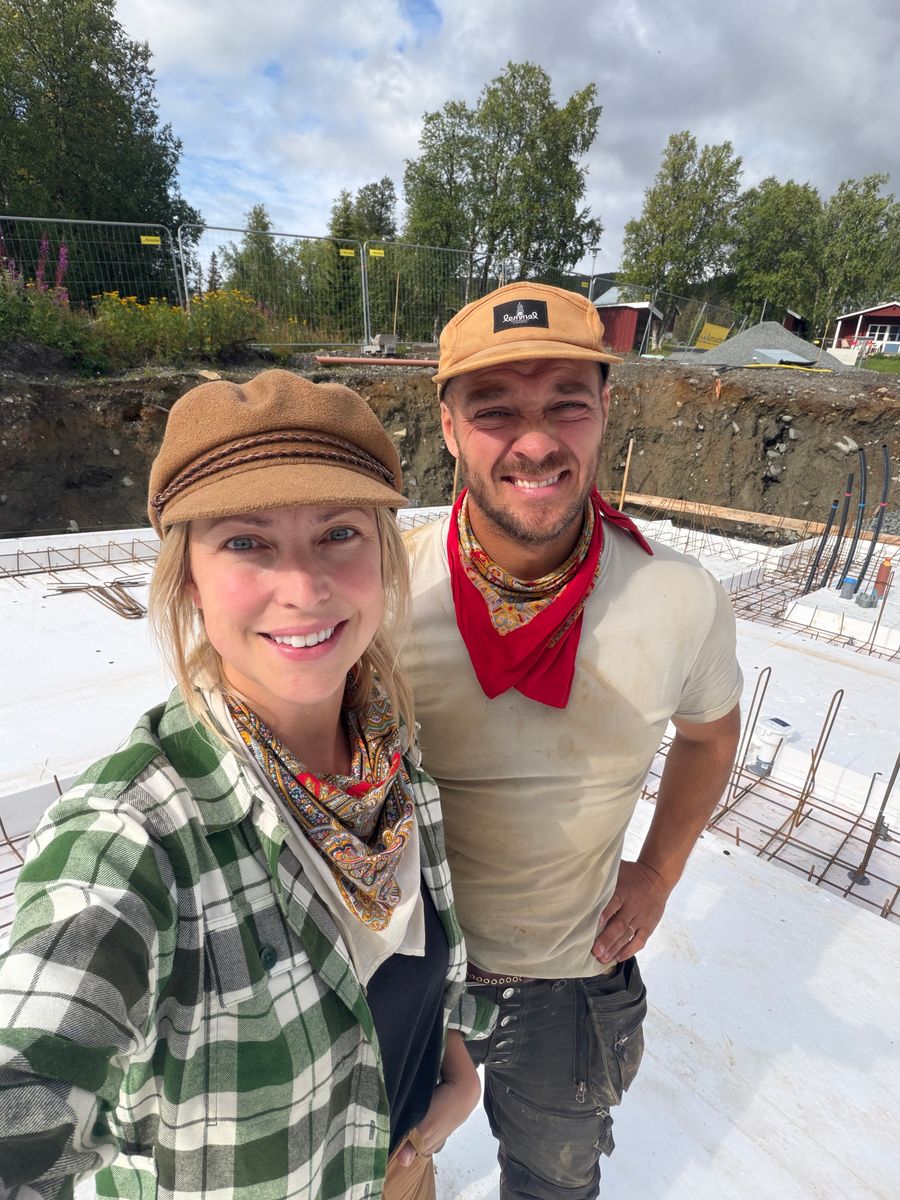 Cecilia och Joakim Engwall ler vid en husbyggarbetsplats med grundplatta utomhus