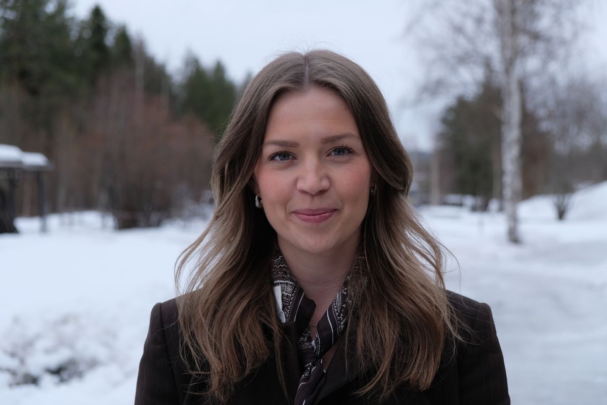 Leende kvinna utomhus en vinterdag med snö och träd i bakgrunden