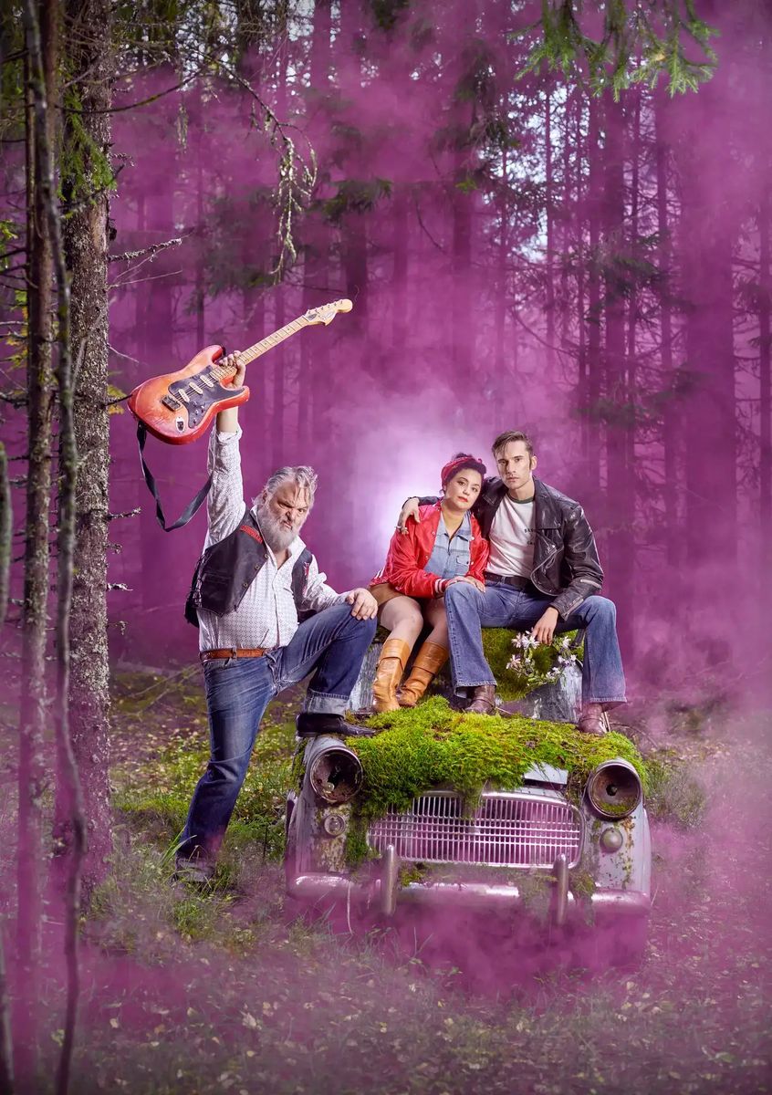 Rockigt gäng poserar på gammal mossig bil i skogen, omgivna av dramatisk lila rök
