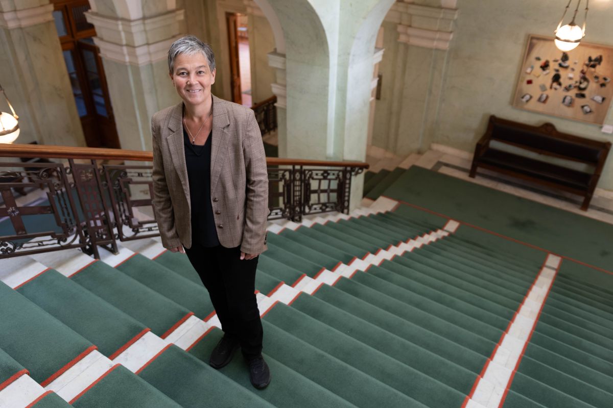 Person i kavaj poserar på bred trappa med grön matta i historisk interiör
