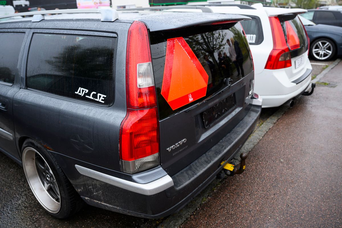 Två Volvo kombibilar på regnig parkering med röda varningstrianglar bak