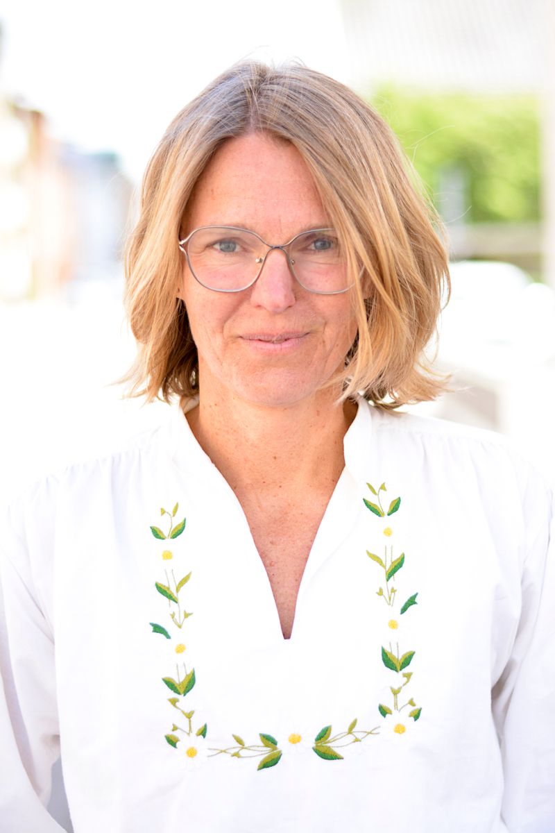 Leende kvinna med glasögon i vit blus med blombroderi utomhus