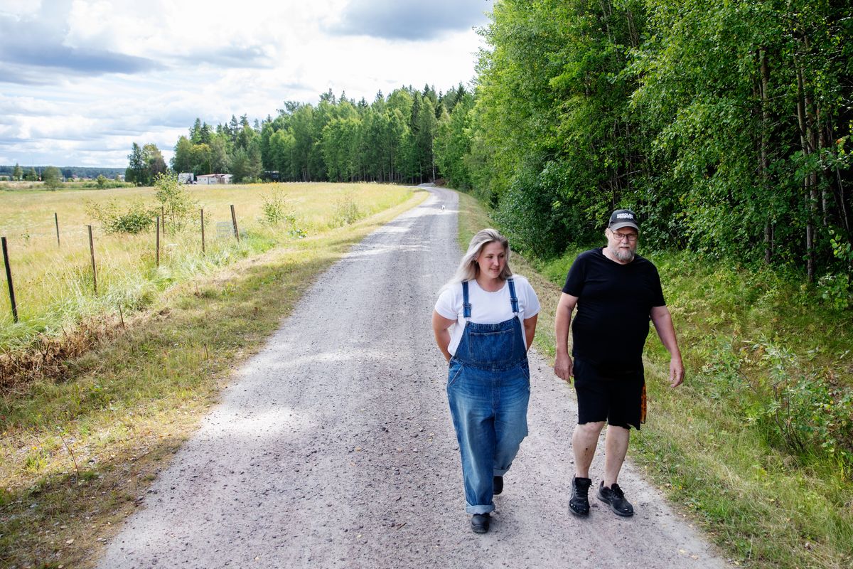 Man och kvinna går på lantlig grusväg omgiven av skog och öppna fält