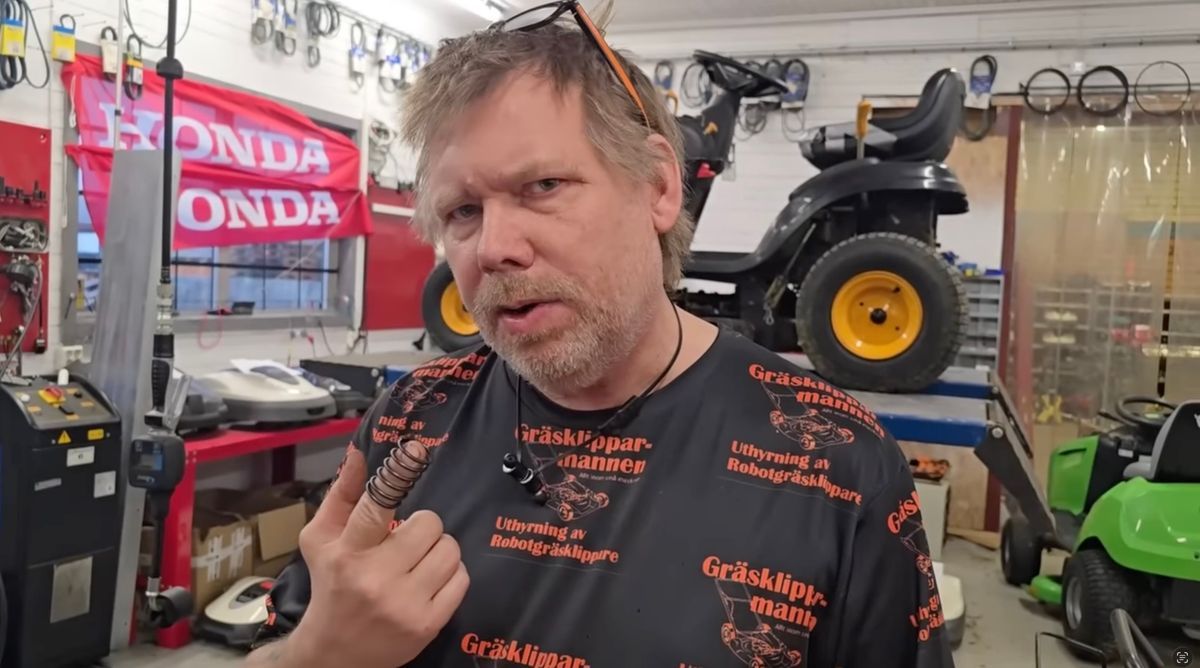 NIcke Johansson i verkstad håller upp en fjäder framför en åkgräsklippare