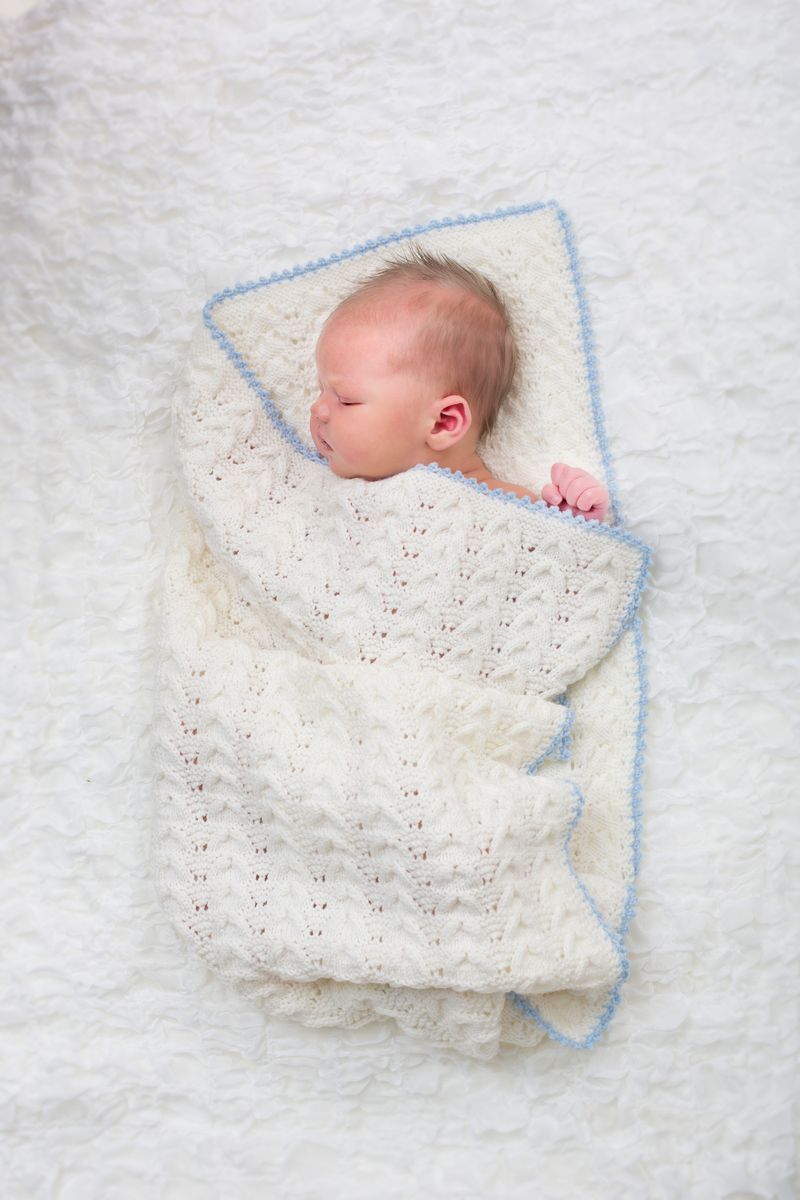 Nyfött barn insvept i vit stickad babyfilt på mjuk vit bakgrund