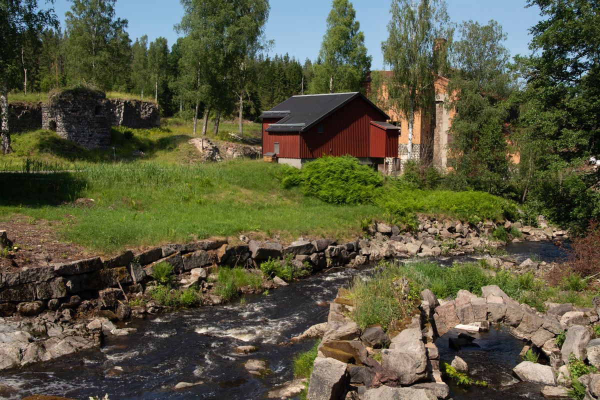 Vatten med stenar framför rött hus och gamla ruiner i lummigt landskap