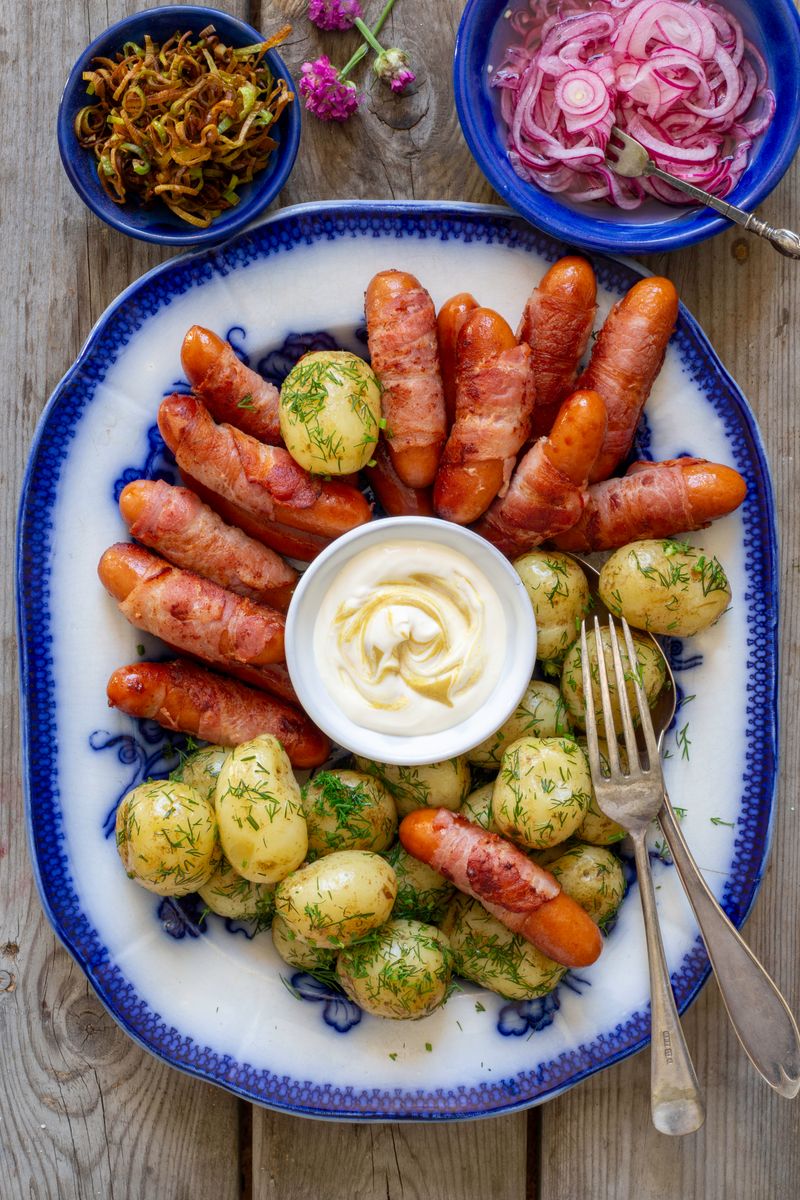Baconrullad prinskorv med potatis, senapskräm, picklad rödlök och framröstad purjolök.