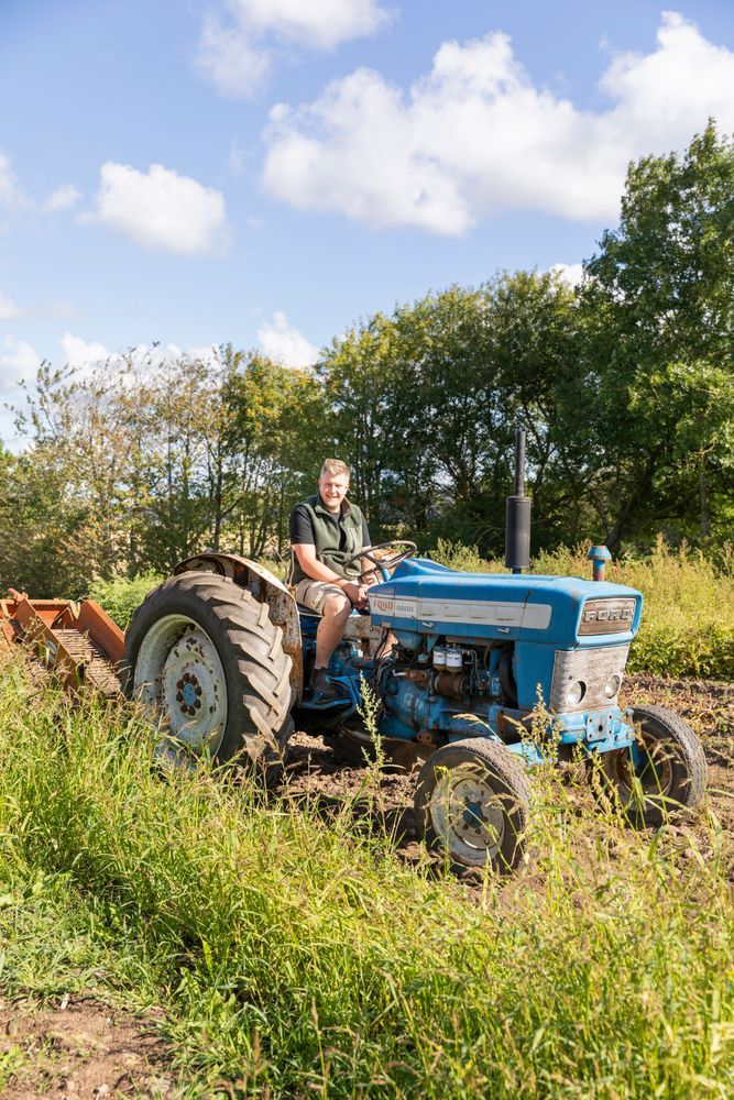 Tommy kör blå traktor på åker under klarblå himmel.
