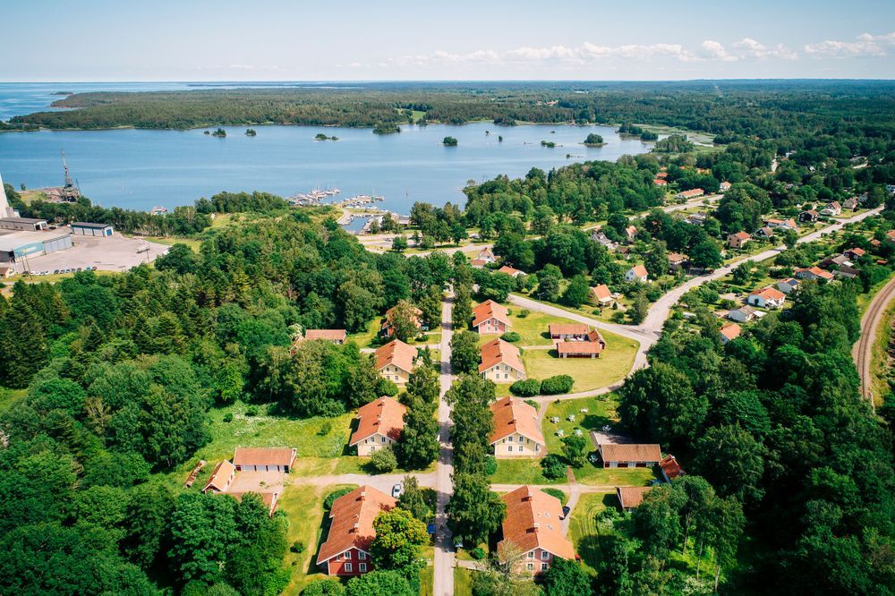 Flygbild över en grönskande by vid en sjö med skog i bakgrunden.
