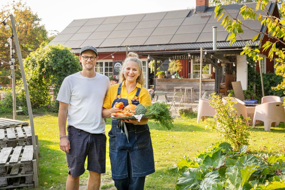 Marcus Nordgren och Lisa Lemke står utanför ett sin gårdspizzeria, Lisa håller en tallrik med grönsaker.