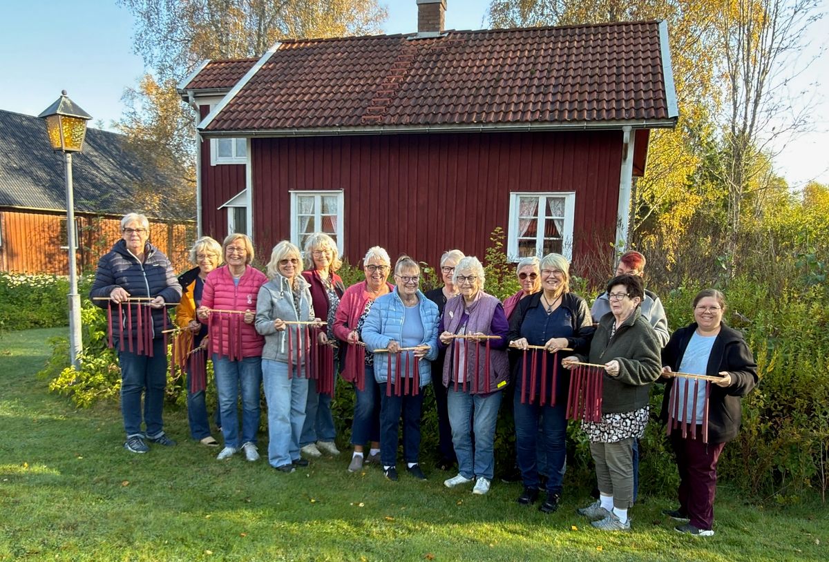 Grupp personer framför rött trähus håller upp färggranna ljus.