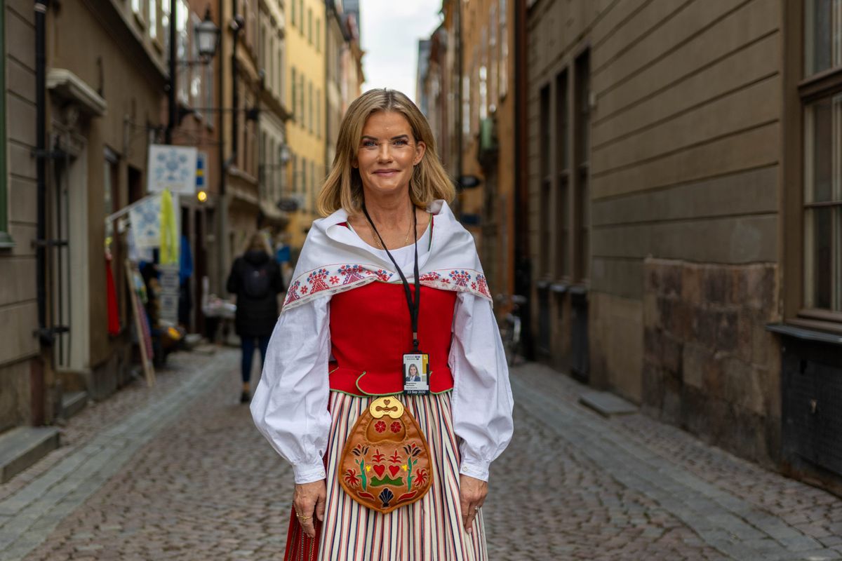 Kvinna i svensk folkdräkt står på kullerstensgata mellan äldre stadshus