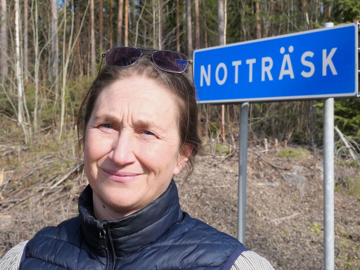 Kvinna utomhus framför en blå vägskylt med texten Notträsk