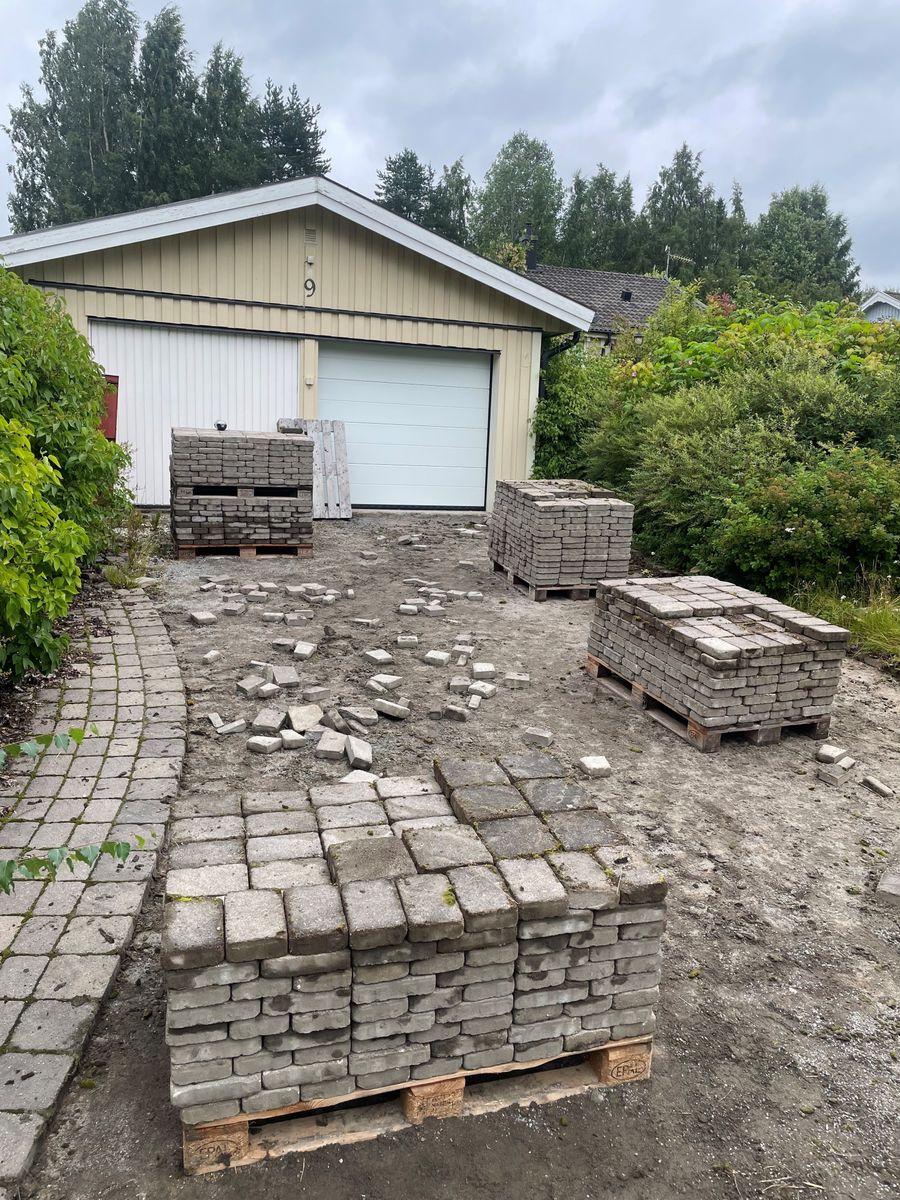 Uppfart framför garage med staplade markstenar och pågående stenläggning