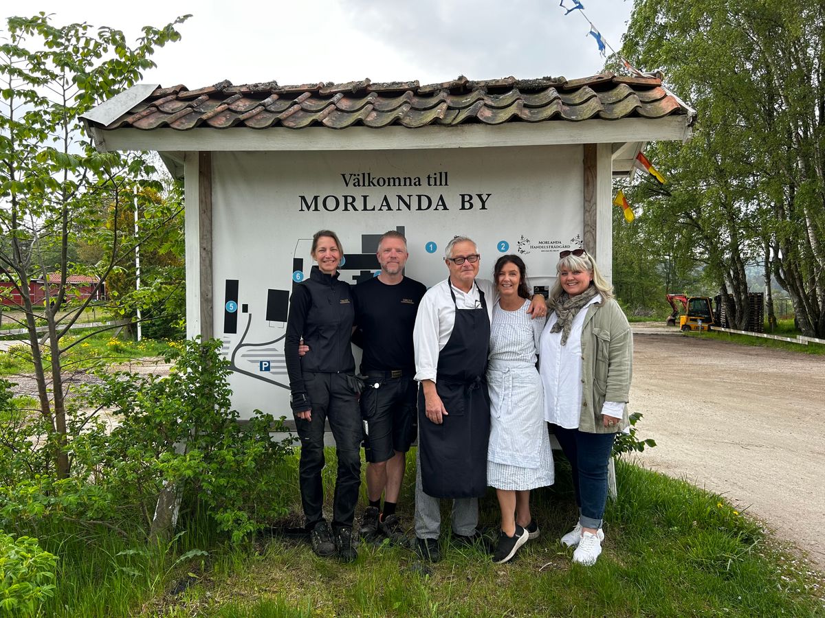 Fem personer ler framför skylten Välkomna till Morlanda By utomhus; Från vänster: Maria Hildemar och Andres Henriksson, Andres och Marina Päärt och Victoria Sjöqvist