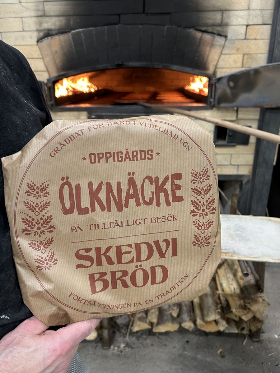 Person håller paketet Oppigårds ölknäcke framför en vedeldad ugn med brinnande eld